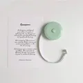 Close-up of mint green mini retractable tape measure with white fiber scale on a desk - Green