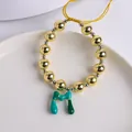 Detalle de pulsera de cuentas en oro 18K con colgante de letra M en esmalte verde - Letra M