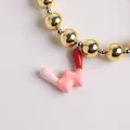 Pulsera de cuentas chapada en oro de 18K con dije de esmalte rojo y rosa en fondo blanco - Letra W