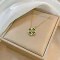 Foldable gold clover necklace with heart shaped green crystals on white satin - Emerald