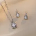 Primer plano de elegante conjunto de collar con colgante halo y pendientes sobre satén aura - Conjunto de collar y pendientes plateados