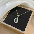 Elegante Goldkette mit birnenförmigem Smaragdanhänger und Zirkon-Halo auf Samtuntergrund - Wassertropfen Smaragd Halskette / Gold
