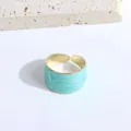 Detalle de esmalte jaspeado azul claro en un anillo ancho abierto de metal dorado - Verde Lago