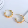 Detalle de pendientes de aro dorados con bordes ondulados y esmalte naranja intenso - Naranja