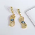 Detalle de pendientes de ojo turco chapados en oro 18K con textura ondulada sobre fondo blanco - Negro