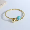 Detailed shot of twisted rope gold cuff bracelet featuring evil eye bead and gold ball charm - Lake Green