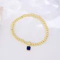 Macro detail of 18k gold plated beaded bracelet with blue square zircon birthstone charm - September (Sapphire Zirconia)