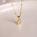 Collar con colgante letra D burbuja dorada 18K con cadena de bolas en fondo rosa suave - Letra D