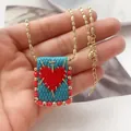Macro shot of 18K gold woven square pendant necklace featuring a red heart and golden cross - Teal