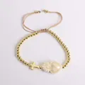 Detailed shot of gold bead bracelet with cross charm and heart pendant on beige cord - White