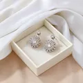 Detailed view of silver flower earrings with radiant stones in a white jewelry box - Rotating Earrings / Steel