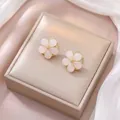 Vista macro di orecchini a fiore rosa con dettagli dorati su velluto champagne - Orecchini pendenti con perla bianca
