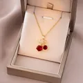 Détail d'un collier pendentif cerise dorée avec zircons rouges dans son écrin cadeau - Zirconium Rouge Cerise