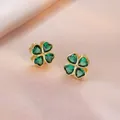 Elegant gold four-leaf clover stud earrings with deep green gemstones on pink silk - Emerald Green Rotating Earrings