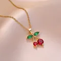 Élégant collier pendentif cerise dorée avec pierres rouges et vertes sur fond de satin rose - Collier Cerise (X2664)