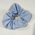 Light blue fabric scrunchie with cream trim and floral tag on a white stone background - Light Blue
