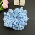 Chouchou fleuri bleu clair avec détails plissés sur fond de cuir noir texturé - Floral Bleu