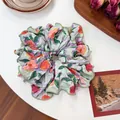 Elegant floral scrunchie in pink and orange print with green edge on a white desk - Orange