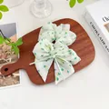 Detail eines floralen Chiffon-Scrunchie mit grüner Schleife und Perle auf Holztablett - Band-Haargummi