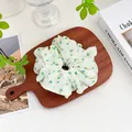 Detail eines weißen Stoff-Haargummis mit gelben Blumen auf einem Holztablett - Punktierter Haargummi