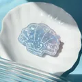 Detailed view of a blue and purple shell hair clip with bow pattern on a white dish - Shell
