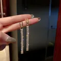 Dettaglio di orecchini a nappa dorati con zirconi cubici tenuti tra le dita con eleganza - Orecchini a Pendolo con Nappa a Catena Oro