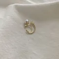 Detalle del pendiente de clip doble C dorado con perlas blancas sobre tela blanca - Clip de Oreja de Perla Dorada / Dorado