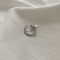 Detalle macro de un pendiente de cartílago plateado con perlas en tela blanca - Clip de Oreja de Perla Dorada / Plateado