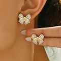 Elegant gold bow earrings with white pearls and rhinestones on model ear - Pave Pearl Rhinestone Bow Style (EHSM0144)