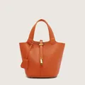Detailed macro view of orange textured bucket bag with golden padlock and leather straps - Orange