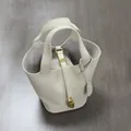 Detailed 45-degree view of beige pebble grain leather bucket bag with gold hardware and lock - White