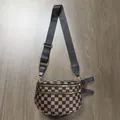 Detail view of checkerboard pattern crossbody bag with golden zippers on wooden floor - Coffee Plaid