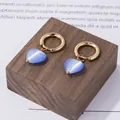 Goldene Creolen mit blauen Katzenaugen-Herzanhängern auf Holzsockel Display - Blaue Katzenaugenstein Herzohrringe