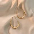Minimalistische gouden druppeloorbellen met spiegelglans op luxe champagne zijden stof - Goud