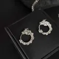 Silver dragon hoop earrings with detailed relief sculpture on a black jewelry stand - Silver