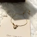 Elegante bracciale con ciondolo a cuore dorato, catena regolabile e inserto perlato - Bracciale Con Perline a Cuore