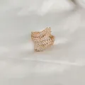 Dettaglio di un anello a piuma dorato con zirconi bianchi lucidi su seta bianca morbida - Squisito Anello d'Oro
