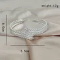 Bracciale a piuma argentato con pavé di zirconi su sfondo di seta color champagne - Bracciale Rigido Argento