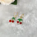 Dettaglio di orecchini a ciliegia rossi con foglie verdi e cerchi dorati su sfondo bianco - Orecchini a ciliegia in smalto rosso lucido (D0922)