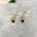 Makroaufnahme von Gold-Kirschohrringen mit roten Steinen und funkelnden Kristallen - Pavé-Strass Doppelball Huggie-Ohrringe