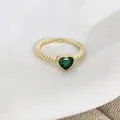 Dettaglio anello dorato con perline e pietra verde a forma di cuore su tessuto bianco - Cuore Verde (Z0133)