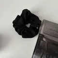 Minimalist black knitted scrunchie with silver logo pendant on a white background - Black