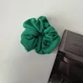 Plush emerald green scrunchie made of towel fabric with a circular gold metal tag - Green