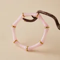 Détail du bracelet en acrylique rose avec anneaux dorés sur une branche de bois - Style Joint de Bambou (AB0081-3) / Rose