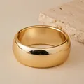 Nahaufnahme der polierten, klobigen Goldmanschette mit Hochglanzfinish auf Travertinstein - Goldener Glatter Bogenstil (AB0096-1)