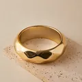 Makroaufnahme eines goldfarbenen breiten geometrischen Armreifs auf beigem Travertinstein - Goldener Geometrischer Polyeder-Schnitt-Armreif (AB0096-3)