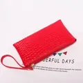 Macro shot of bright red faux leather long wallet with embossed crocodile texture and wrist strap - Red