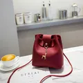 Deep red bucket bag with gold deer pendant and matte leather finish on marble surface - Burgundy