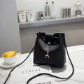 Classic black bucket crossbody bag with golden deer pendant on a white marble tabletop - Black