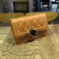 Tan quilted crossbody bag with gold chain strap and geometric metal lock on wood - Brown